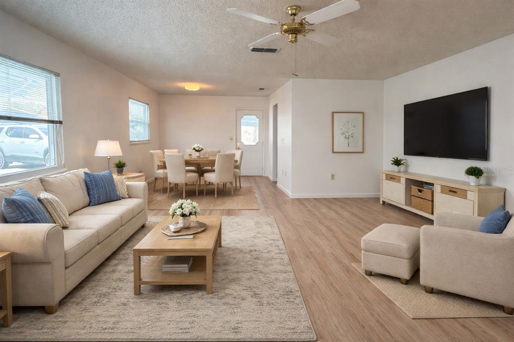 A living room and dining area with light wood flooring, a beige sofa, and television — 9230 SW 101ST LANE, OCALA, FL