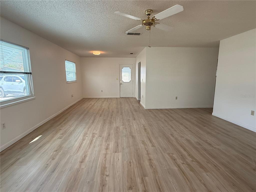An empty living room features light wood-look flooring, white walls, and a ceiling fan — 9230 SW 101ST LANE, OCALA, FL
