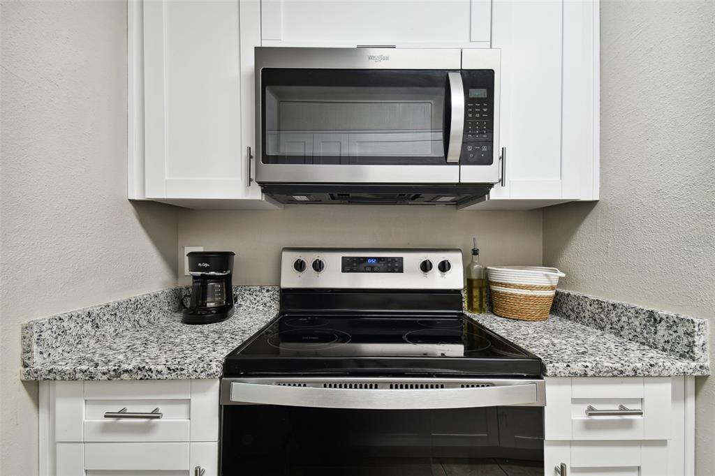 A kitchen features white cabinets, granite countertops, and stainless steel appliances including a microwave and stove — 7504 PRESLEY PLACE UNIT 115 C, TAMPA, FL