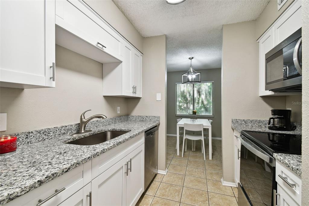 A kitchen with white cabinets, granite countertops, stainless steel appliances, and an adjacent dining area — 7504 PRESLEY PLACE UNIT 115 C, TAMPA, FL
