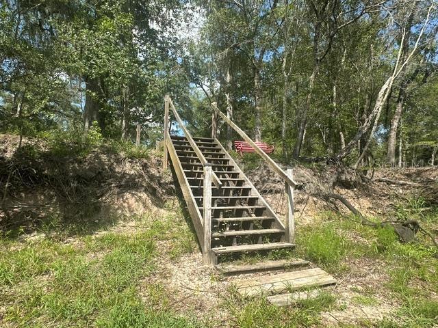 A wooden staircase leads up a grassy embankment toward a red bench in the woods — 1109 NW 78TH AVENUE, BELL, FL