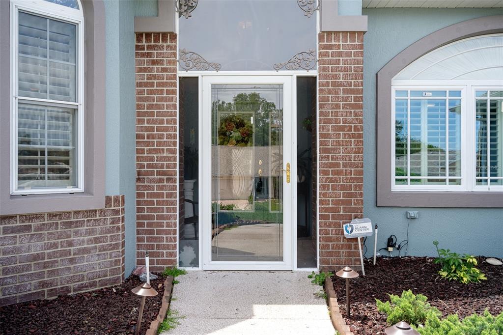 A front entryway features a glass storm door, brick siding, and two windows with shutters — 7450 ALOE DRIVE, SPRING HILL, FL