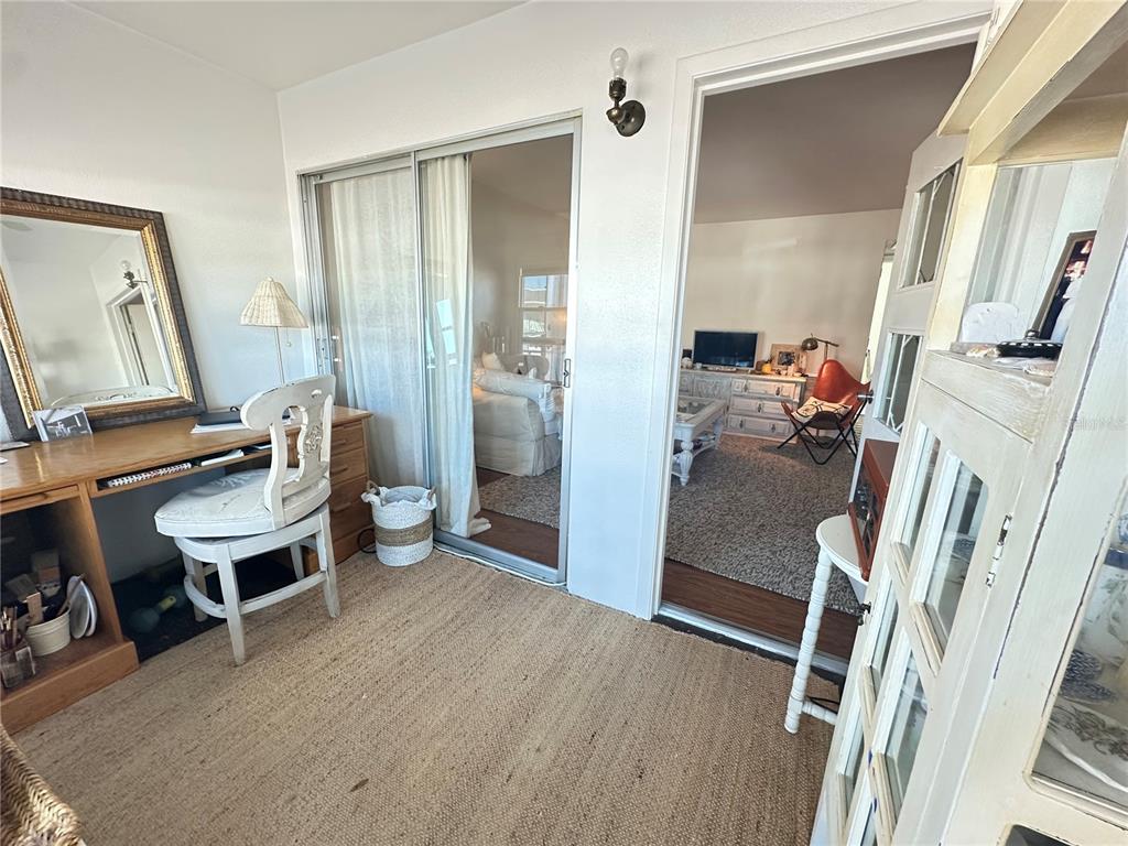 A sunroom features a wooden desk, a white chair, and sliding glass doors to a living room — 1221 DREW STREET UNIT D9, CLEARWATER, FL