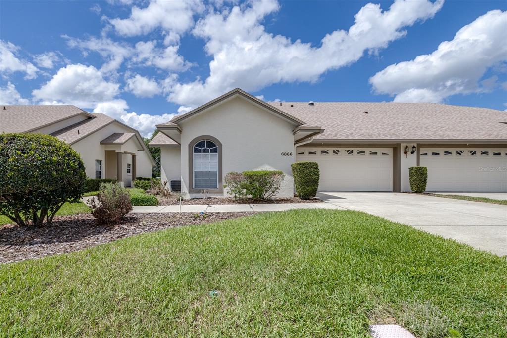 A single-story duplex with a beige stucco exterior, a two-car garage, and a front lawn — 6866 BENDELOW DRIVE, LAKELAND, FL