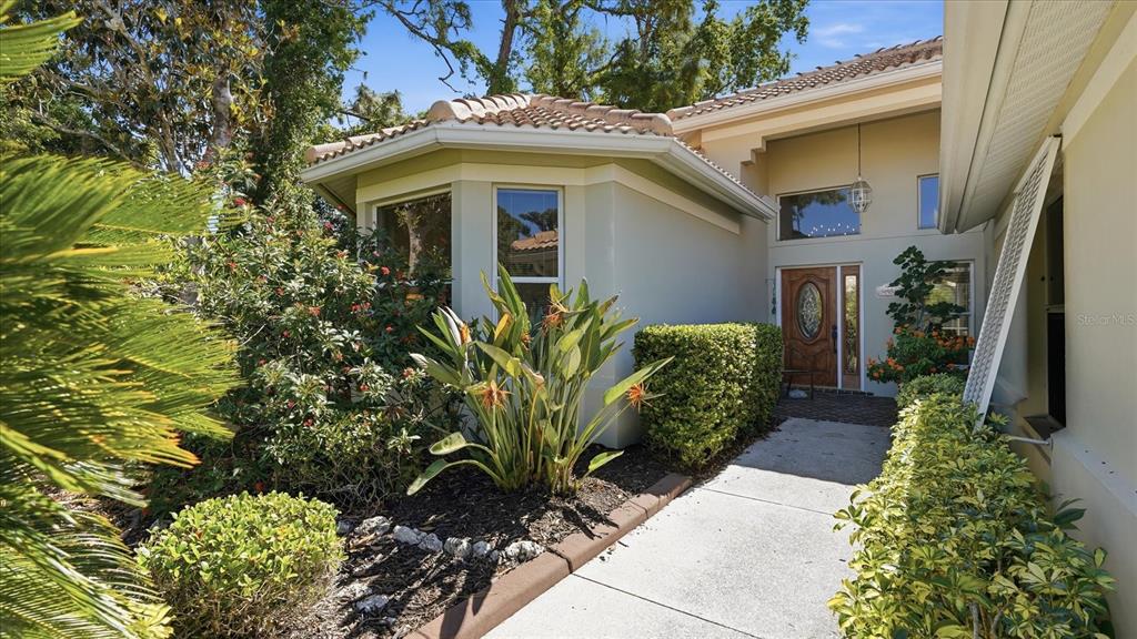 A concrete walkway leads to the front entrance of a house with a tiled roof — 8009 HAMPTON COURT, UNIVERSITY PARK, FL