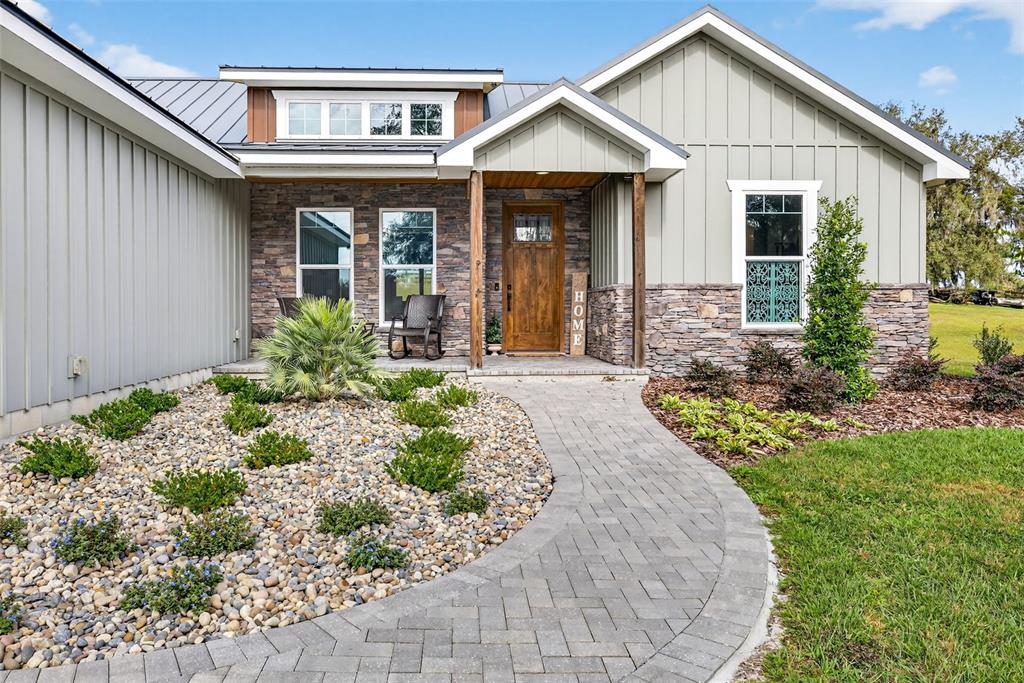 A stone and board-and-batten house exterior features a paved walkway leading to the front door — 32103 RUSTY CREEK TRAIL, DADE CITY, FL