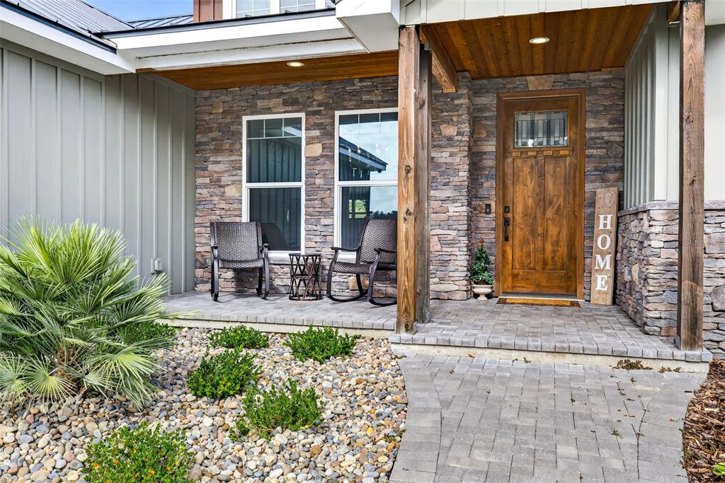 A stone-faced porch features a wooden front door, two rocking chairs, and a stone walkway — 32103 RUSTY CREEK TRAIL, DADE CITY, FL