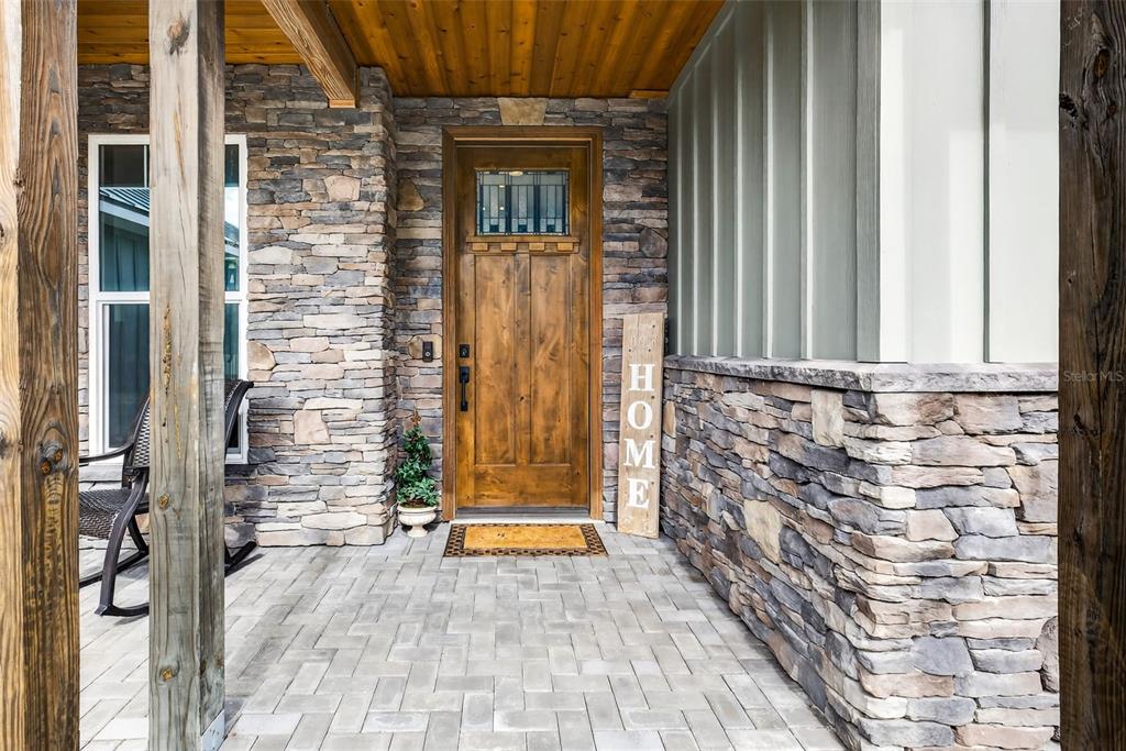 A covered stone porch features a wooden front door, a rocking chair, and a welcome sign — 32103 RUSTY CREEK TRAIL, DADE CITY, FL