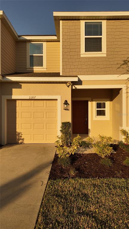 A two-story townhouse exterior features a beige garage, a dark front door, and shingled siding — 2207 PORTRAIT STREET, KISSIMMEE, FL