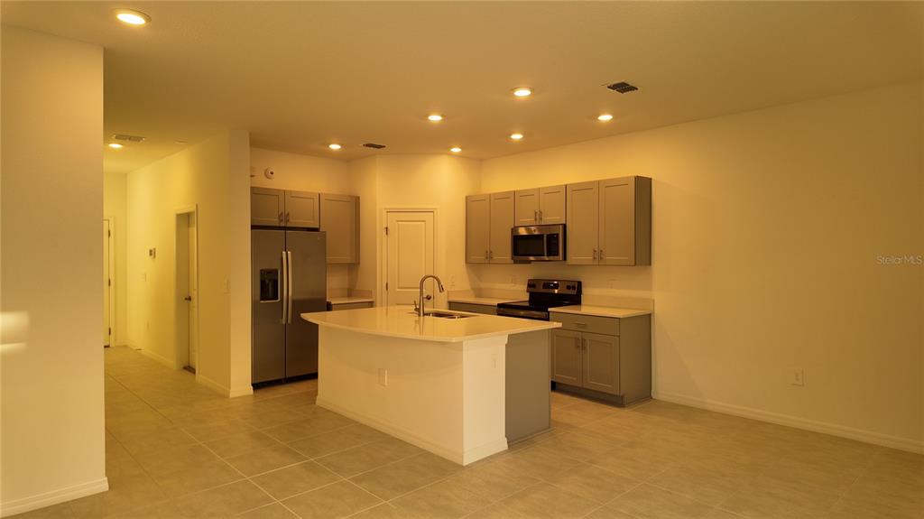 A kitchen features gray cabinets, stainless steel appliances, a center island, and tile flooring — 2207 PORTRAIT STREET, KISSIMMEE, FL