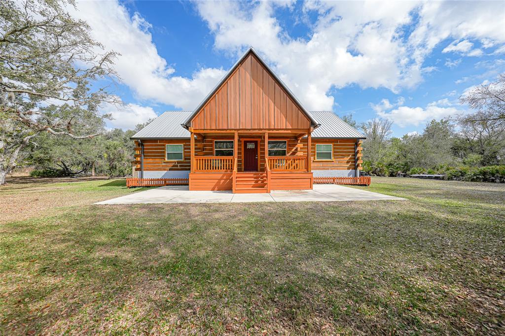 A log cabin with a metal roof and a wooden front porch sits on grass — 9796 SW SOUTHERN DREAMS ROAD, ARCADIA, FL