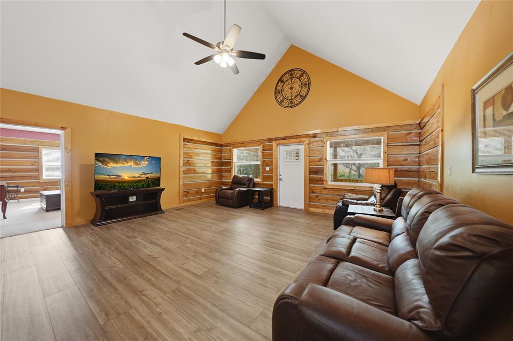 A living room with vaulted ceilings, wood-paneled walls, brown leather furniture, and wood-look flooring — 9796 SW SOUTHERN DREAMS ROAD, ARCADIA, FL
