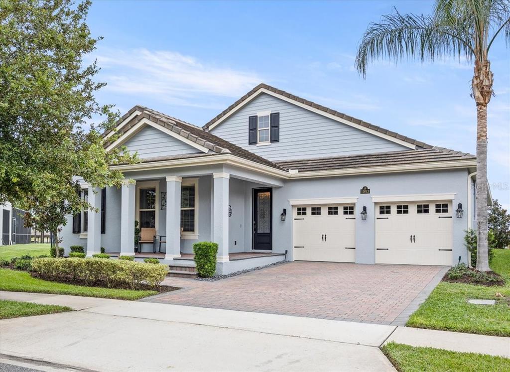 A light blue single-story house with a brick driveway, two-car garage, and covered front porch — 10043 LITTLE ALCOVE LOOP, WINTER GARDEN, FL