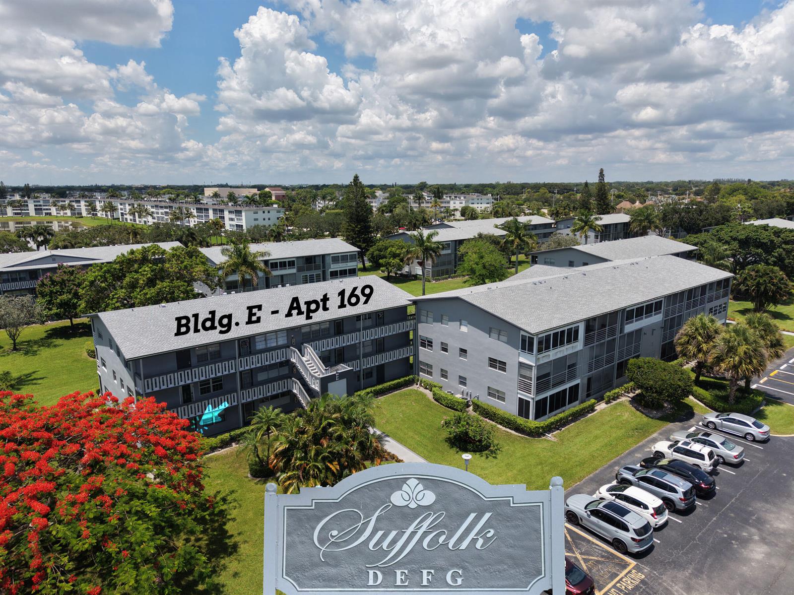 An aerial view shows gray apartment buildings with a parking lot and landscaping — 169 Suffolk E, Boca Raton FL 33434, BOCA RATON, FL