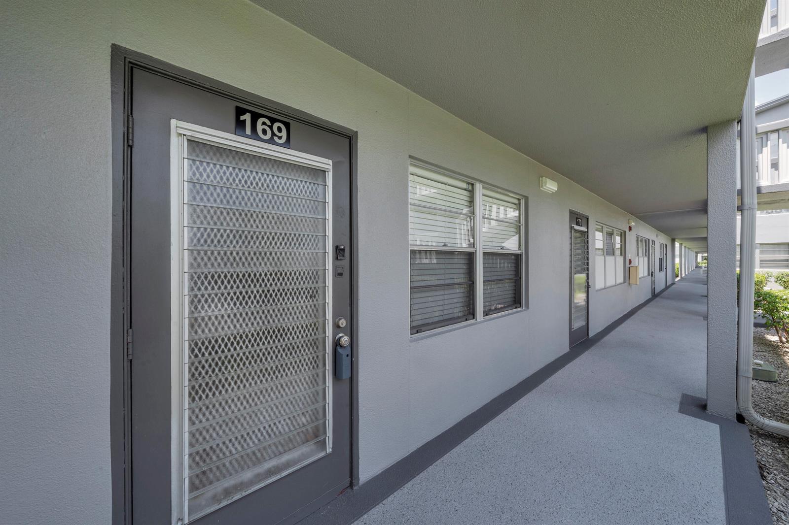 An exterior walkway with gray doors and windows leads past apartment unit 169 — 169 Suffolk E, Boca Raton FL 33434, BOCA RATON, FL