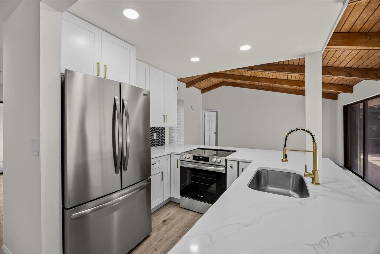 A modern kitchen features white cabinets, stainless steel appliances, a white quartz countertop, and wood-beamed ceilings — 21143 N Escondido Way Way N, Boca Raton FL 33433, BOCA RATON, FL