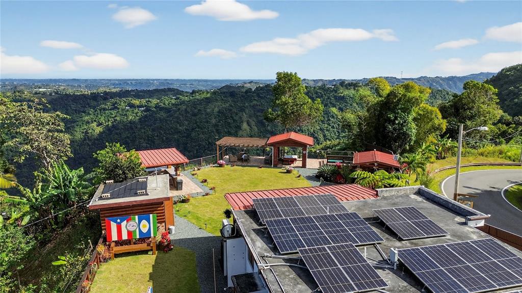 An elevated view shows a house with solar panels, a grassy yard, and mountain scenery — PARCEL A ALTURITAS COLLORES, OROCOVIS, PR