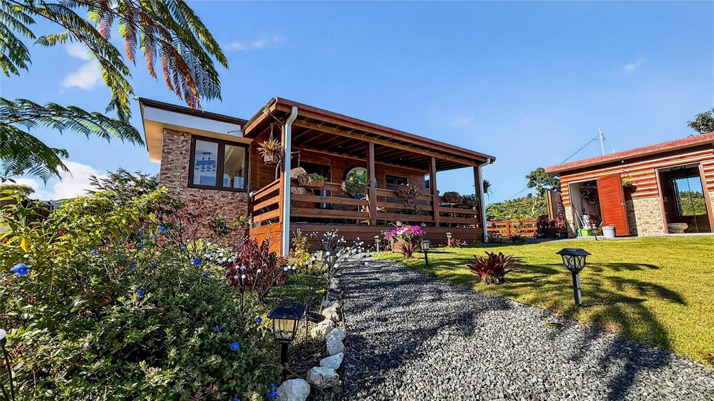 A wooden cabin with a covered porch and gravel path sits on a grassy lawn — PARCEL A ALTURITAS COLLORES, OROCOVIS, PR