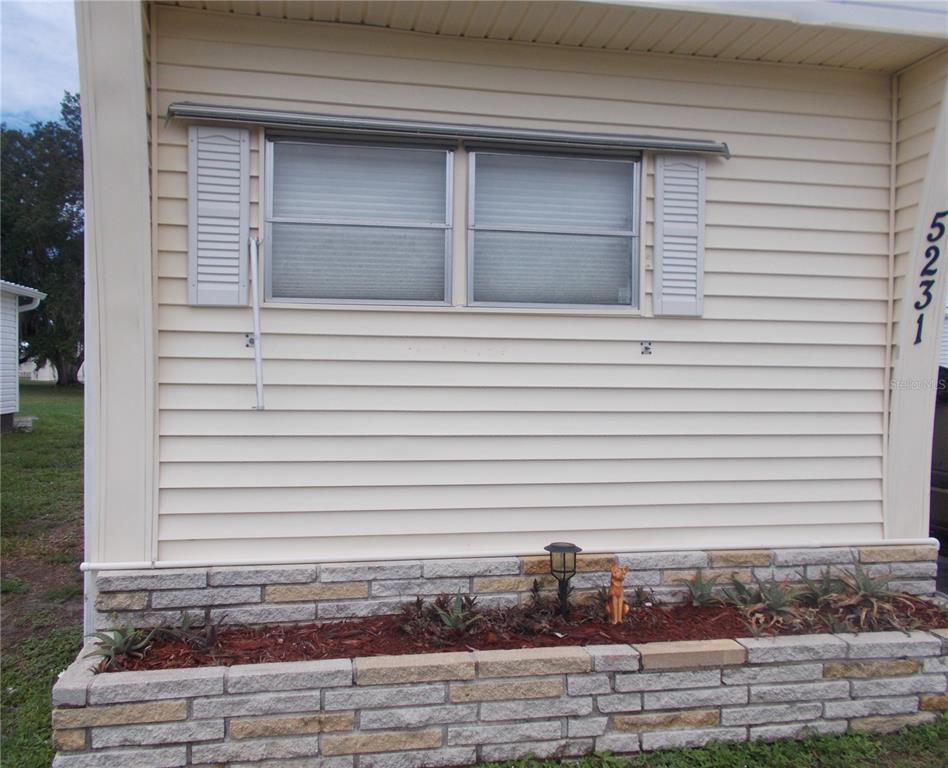 The exterior of a light-colored mobile home features a stone planter and a double window — 5231 PALENA BOULEVARD, NORTH PORT, FL