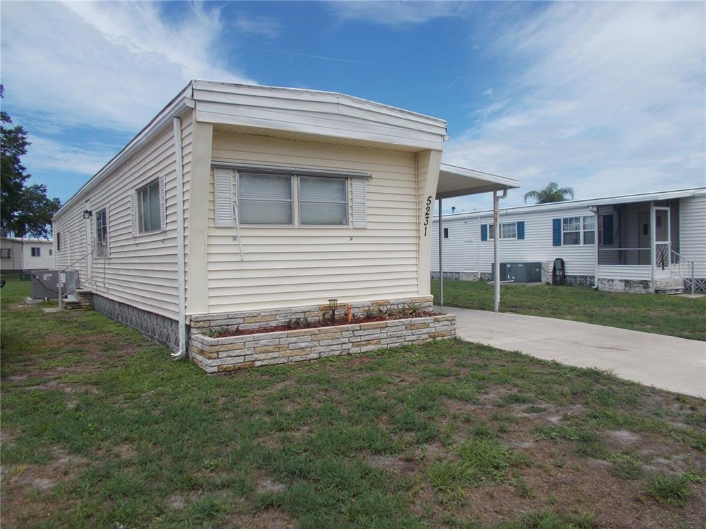 A light-colored mobile home with a stone-accented planter box and a concrete carport — 5231 PALENA BOULEVARD, NORTH PORT, FL