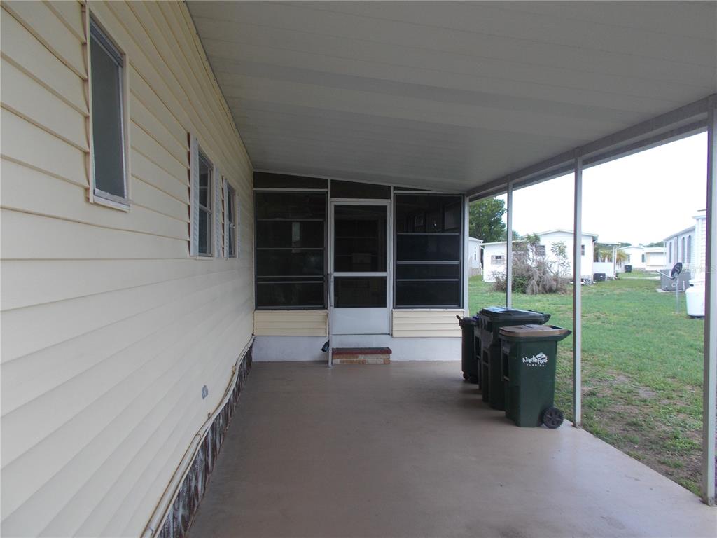 A covered concrete patio sits beside a light yellow mobile home with a screened entrance — 5231 PALENA BOULEVARD, NORTH PORT, FL