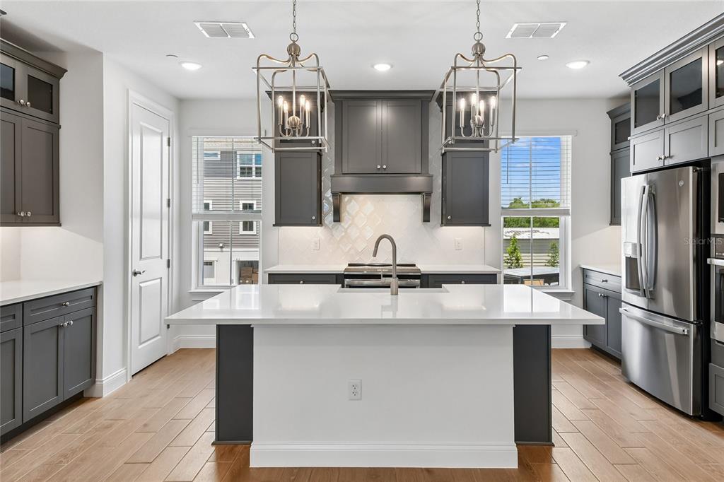 A modern kitchen features dark gray cabinetry, a white quartz island, and two pendant lights — 210 PAQUALA, OVIEDO, FL