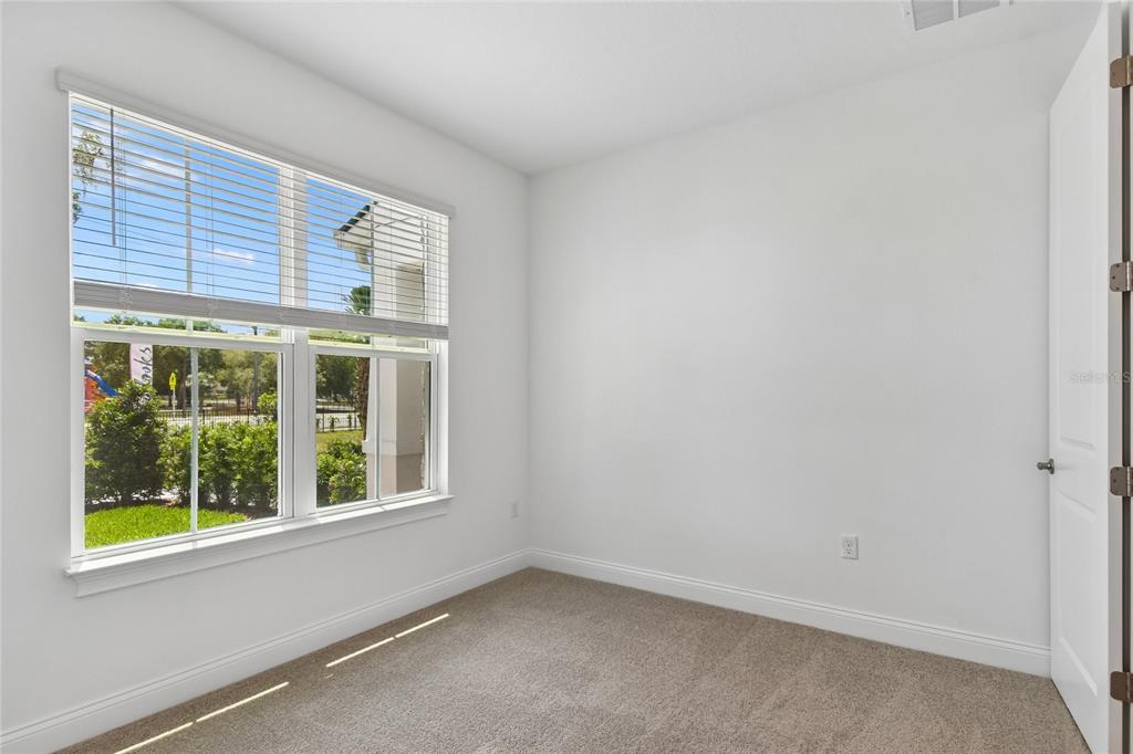 A small, empty room features beige carpeting, white walls, and a large window with blinds — 210 PAQUALA, OVIEDO, FL