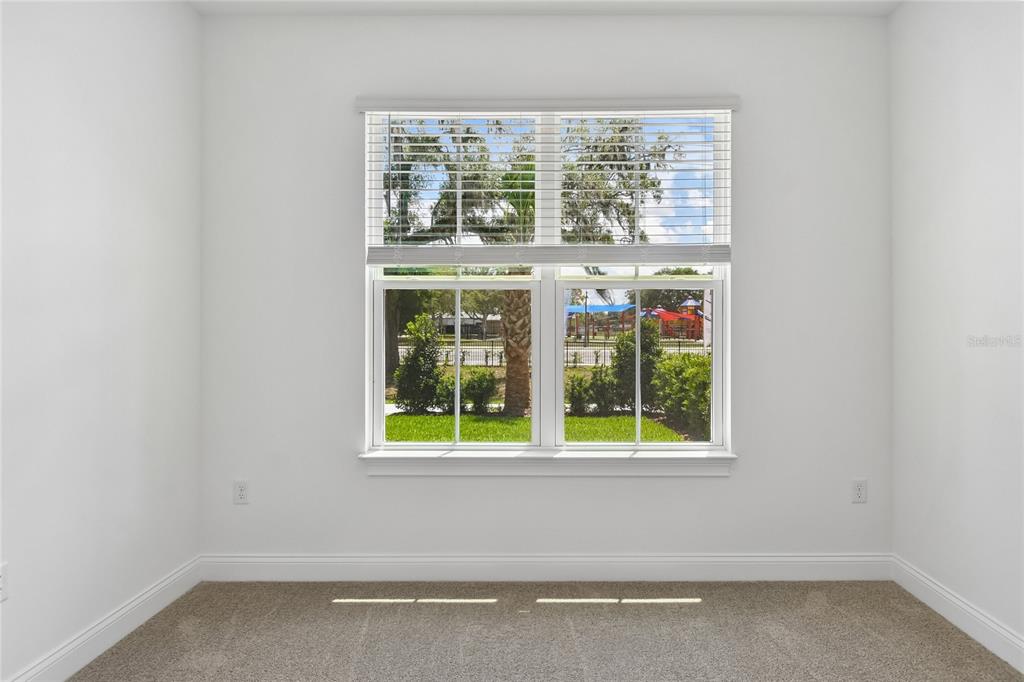 A bright, empty room features white walls, beige carpeting, and a window overlooking a playground — 210 PAQUALA, OVIEDO, FL