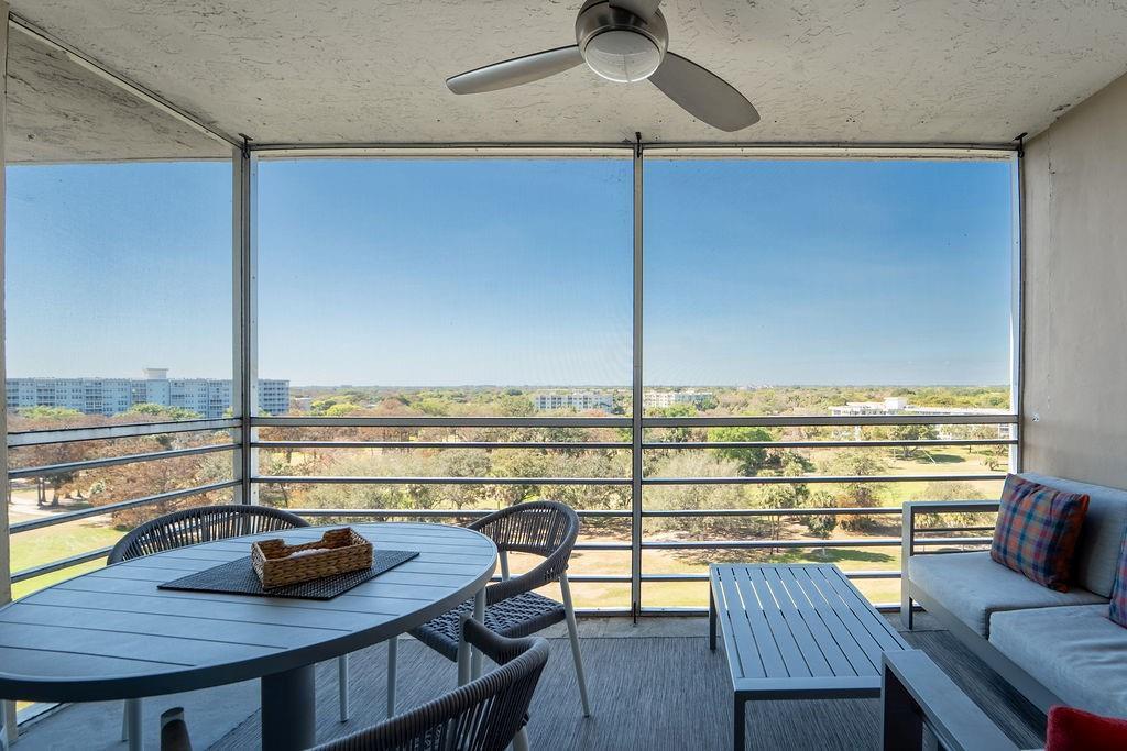 A screened-in balcony features a dining set, lounge seating, and a ceiling fan overlooking trees — 575 Oaks Lane # 1002, Pompano Beach FL 33069, POMPANO BEACH, FL
