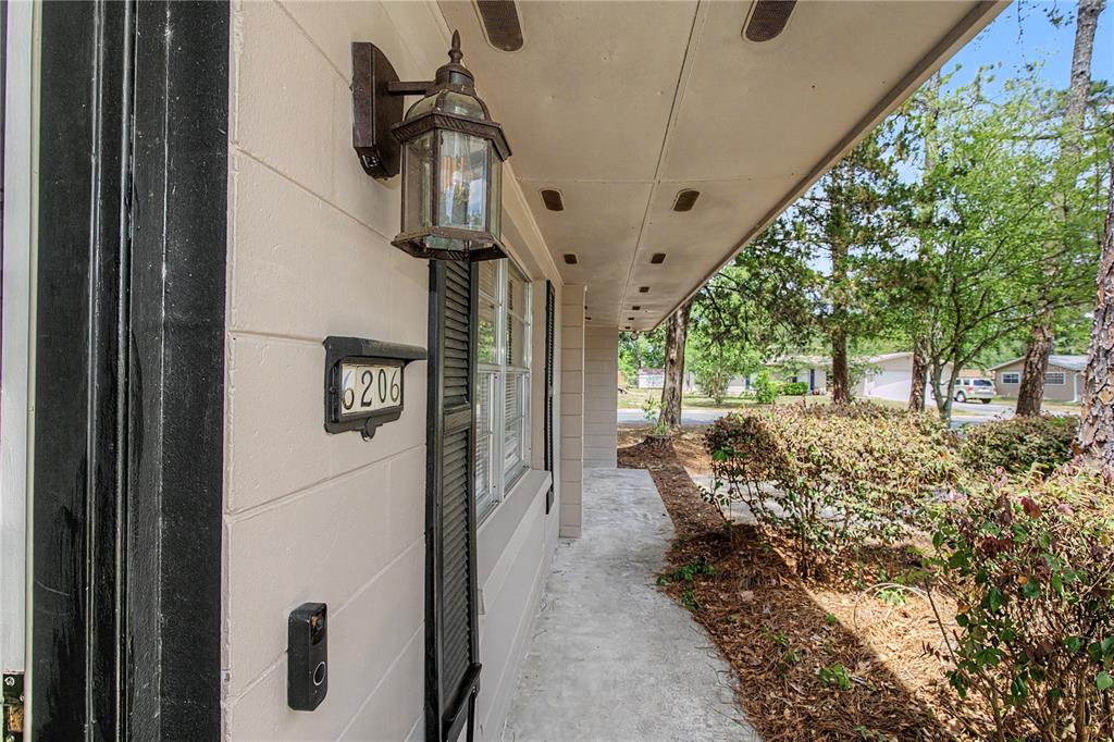 A concrete porch features a wall-mounted house number, a lantern light, and a doorbell camera — 6206 NW 27TH TERRACE, GAINESVILLE, FL