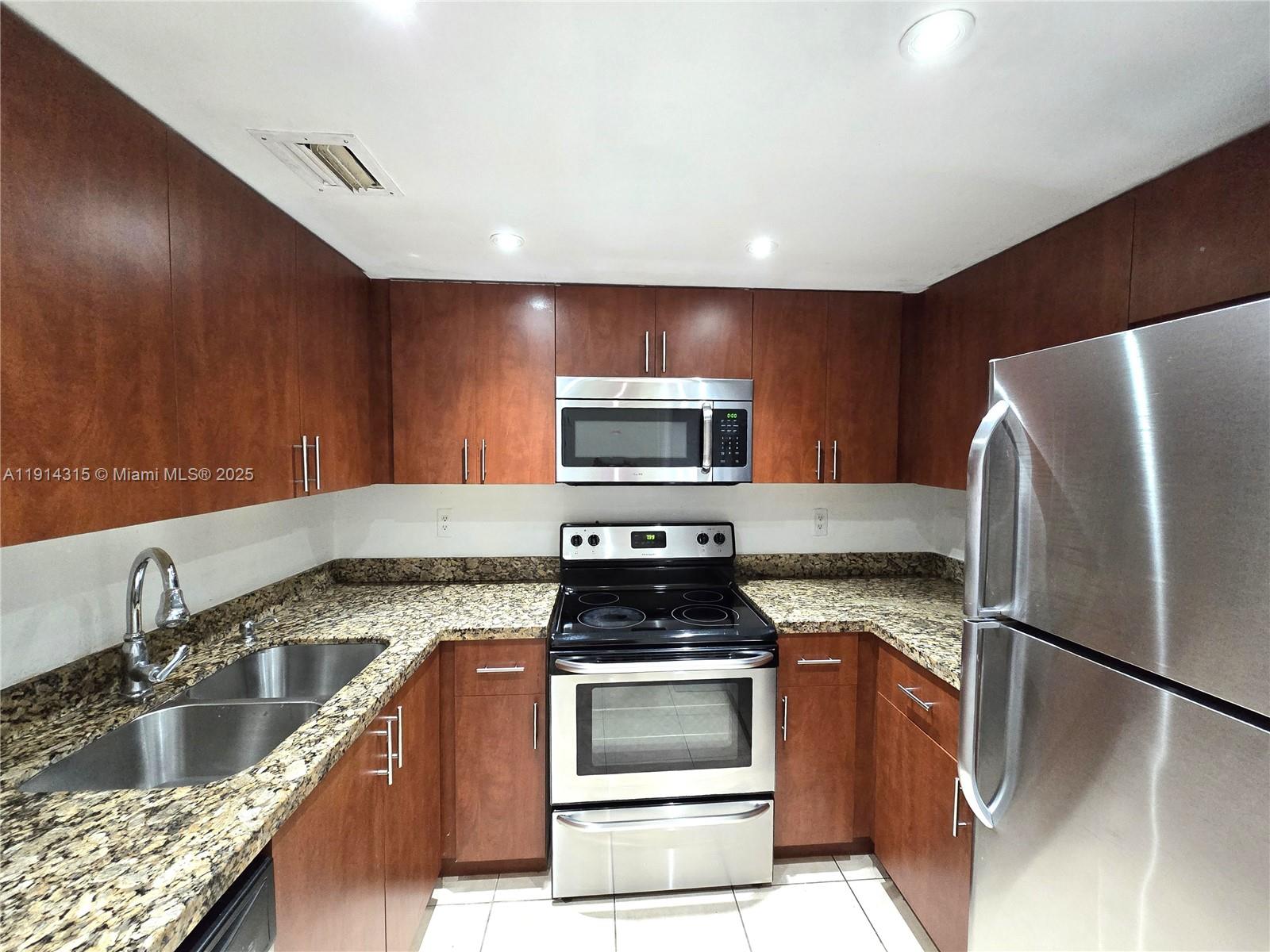 A kitchen features wood cabinets, granite countertops, and stainless steel appliances — 6940 Miami Gardens Dr # 319, Hialeah FL 33015, HIALEAH, FL