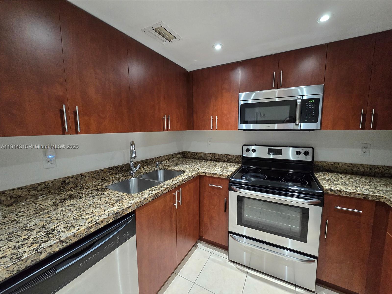 A kitchen features wood cabinets, granite countertops, and stainless steel appliances — 6940 Miami Gardens Dr # 319, Hialeah FL 33015, HIALEAH, FL