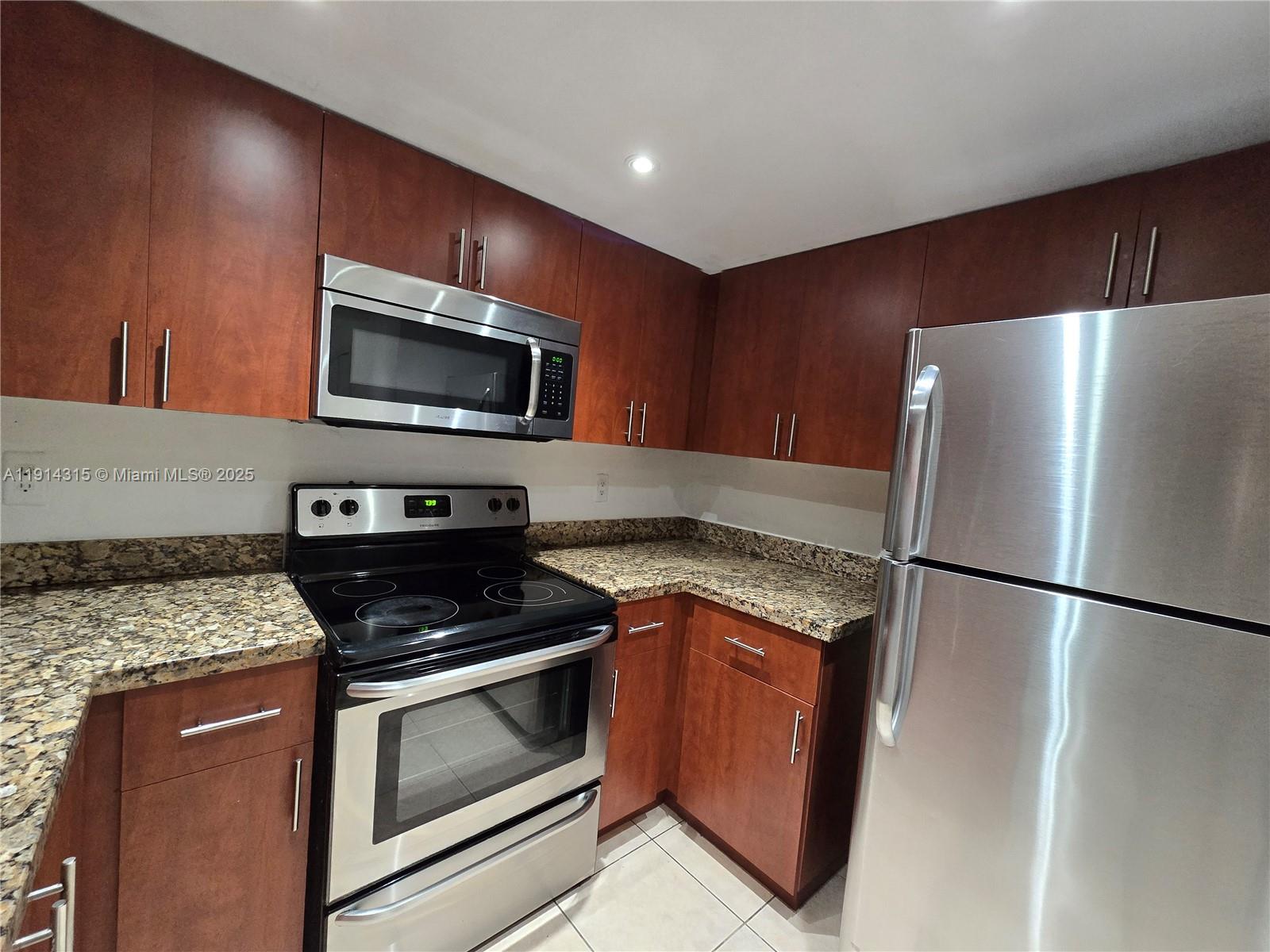 A kitchen features cherry wood cabinets, granite countertops, and stainless steel appliances — 6940 Miami Gardens Dr # 319, Hialeah FL 33015, HIALEAH, FL