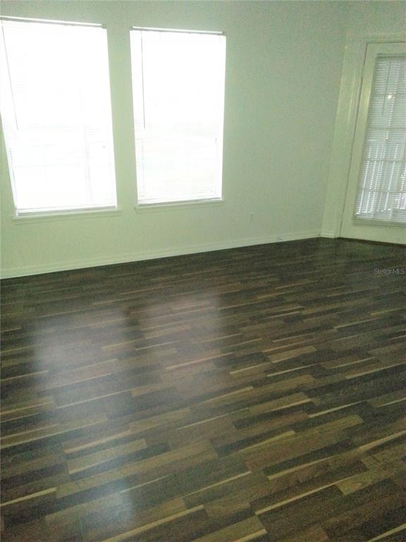 An empty room features dark wood-look flooring, two windows with blinds, and a glass door — 6028 WESTGATE DRIVE UNIT 202, ORLANDO, FL