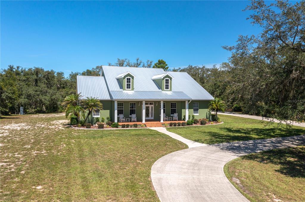 A green two-story house with a metal roof and a concrete driveway sits on grass — 35 STEMBRIDGE ROAD, LAKE WALES, FL