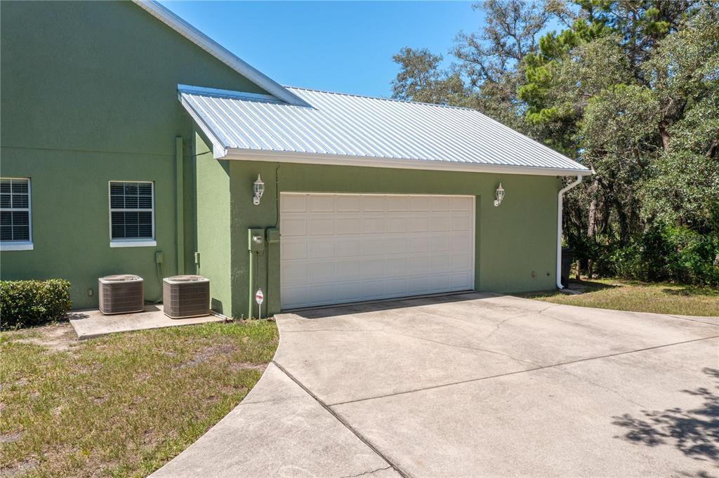 A green house exterior features a two-car garage, a metal roof, and two AC units — 35 STEMBRIDGE ROAD, LAKE WALES, FL
