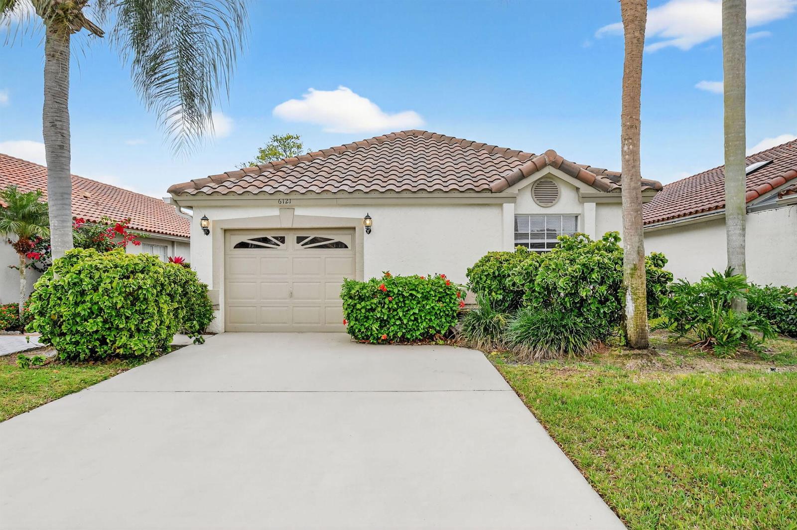 A single-story house with a beige garage, tile roof, and landscaping under a blue sky — 6121 Bay Isles Drive, Boynton Beach FL 33437, BOYNTON BEACH, FL