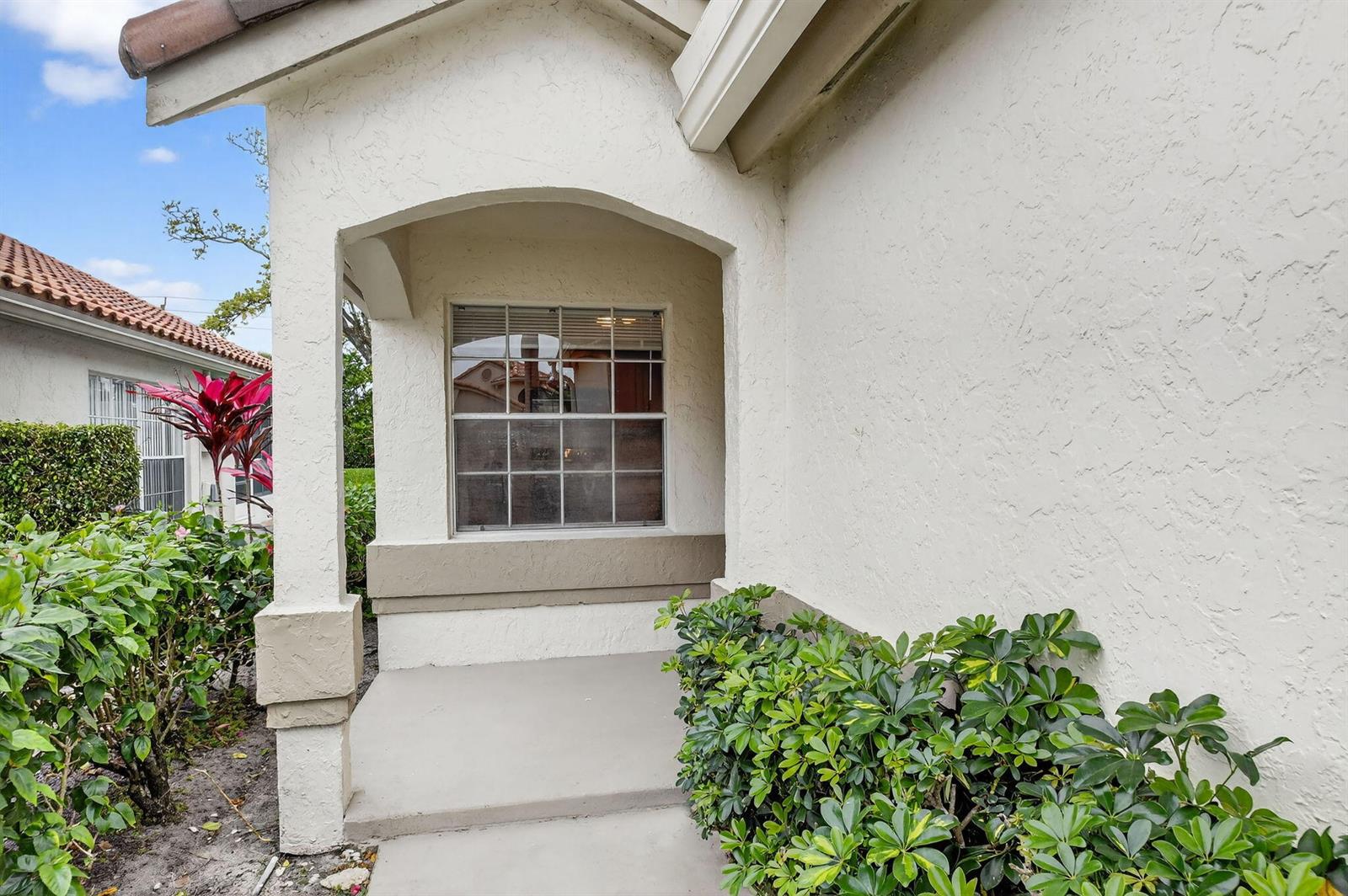 A recessed entryway features a single window, a concrete porch, and surrounding green landscaping — 6121 Bay Isles Drive, Boynton Beach FL 33437, BOYNTON BEACH, FL