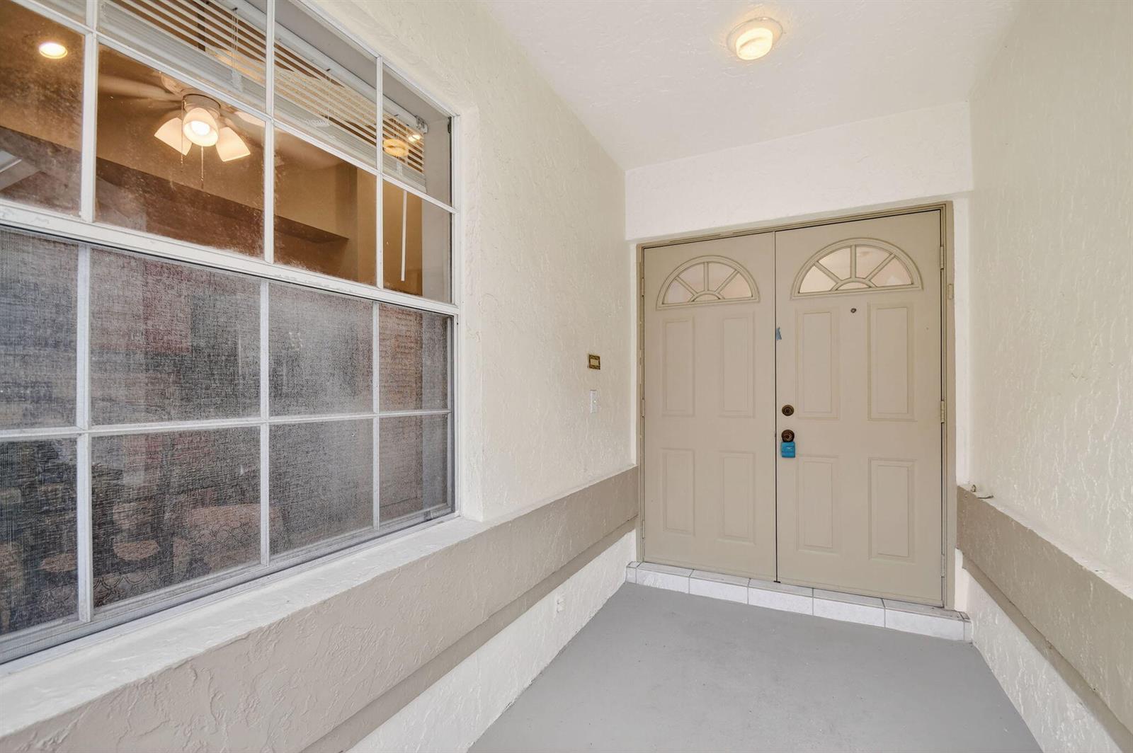 A covered entryway features a large window, a light-colored wall, and double front doors — 6121 Bay Isles Drive, Boynton Beach FL 33437, BOYNTON BEACH, FL