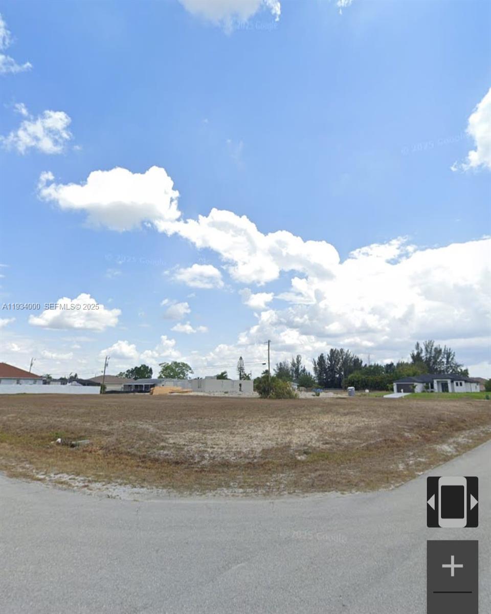 A vacant, grassy residential lot is shown under a bright, cloudy blue sky — 302 NE 10 ST, Cape Coral FL 33909, CAPE CORAL, FL