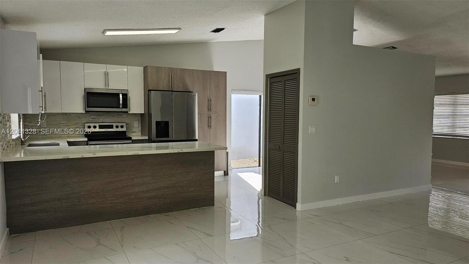 A modern kitchen features white and wood-toned cabinetry, stainless steel appliances, and light-colored tile flooring — 14470 SW 96th Ter, Miami FL 33186, MIAMI, FL