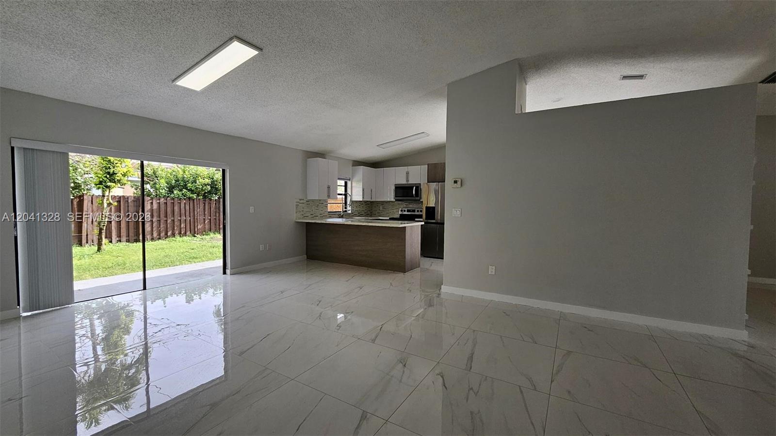 A bright living area features white marble-look tile floors, a kitchen island, and sliding glass doors — 14470 SW 96th Ter, Miami FL 33186, MIAMI, FL
