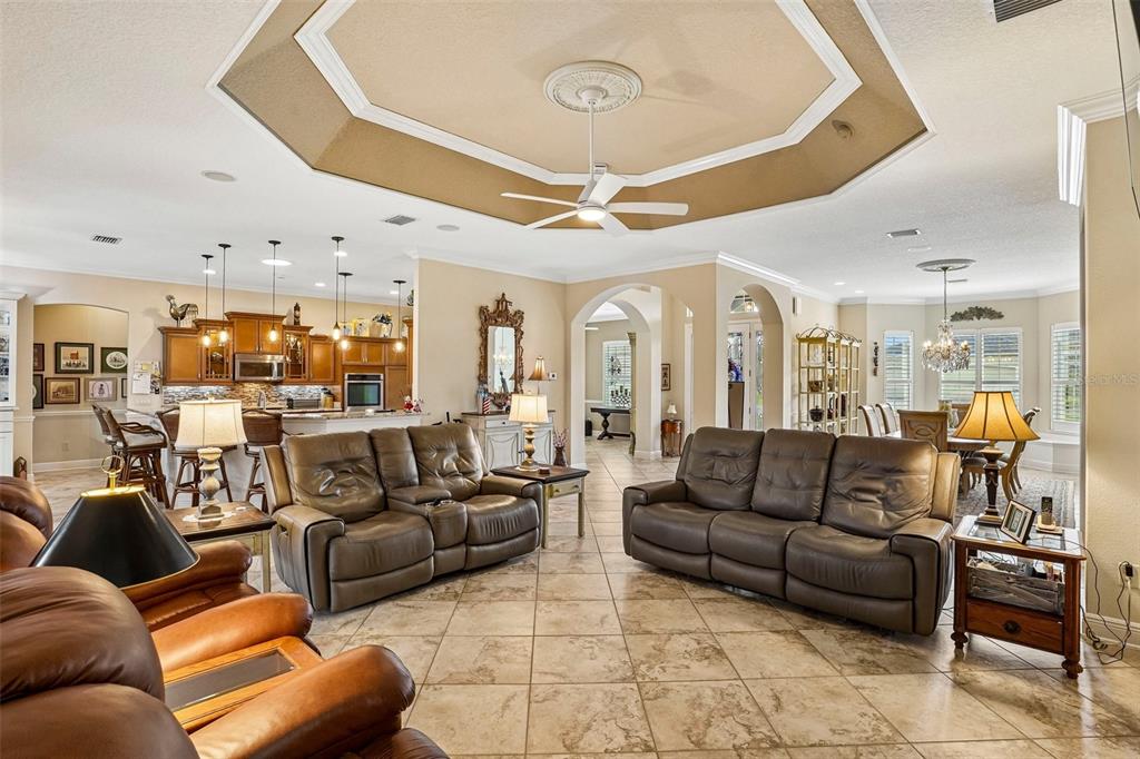 An open-concept living room features a tray ceiling, tile flooring, and leather furniture — 1404 BRIER CREEK CIRCLE, THE VILLAGES, FL