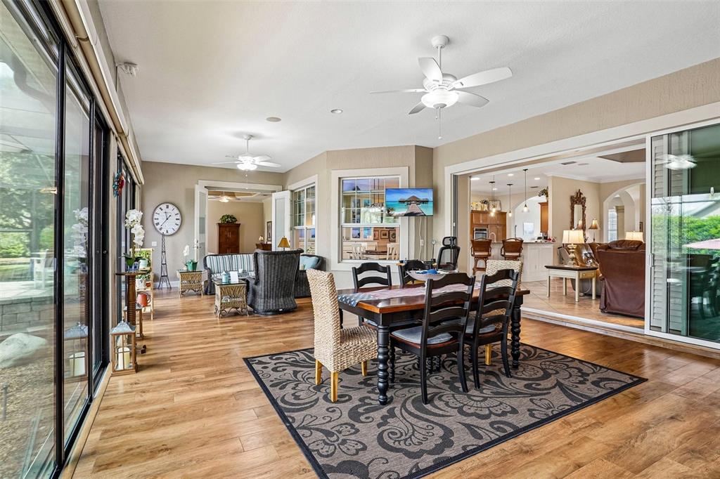 A sunroom with wood-look flooring, a dining set, and sliding glass doors to the interior — 1404 BRIER CREEK CIRCLE, THE VILLAGES, FL