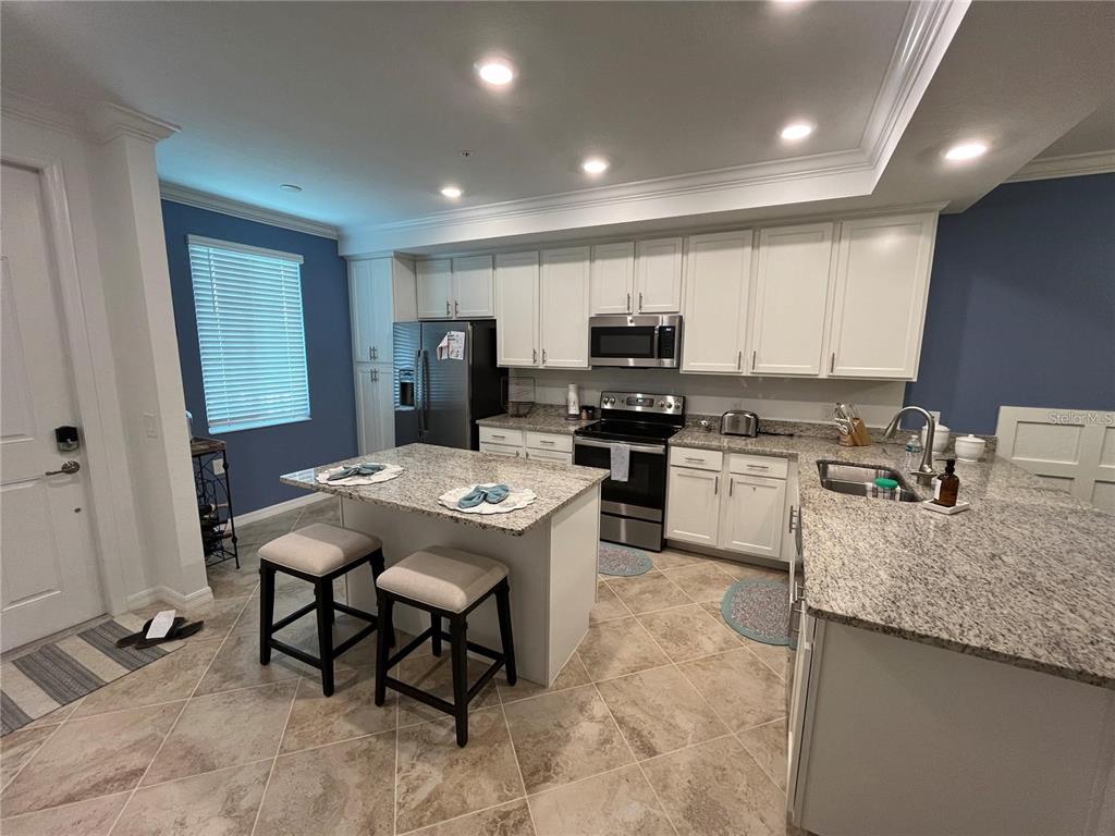A kitchen features white cabinetry, granite countertops, a central island with stools, and tile flooring — 14091 HERITAGE LANDING BOULEVARD UNIT 124, PUNTA GORDA, FL