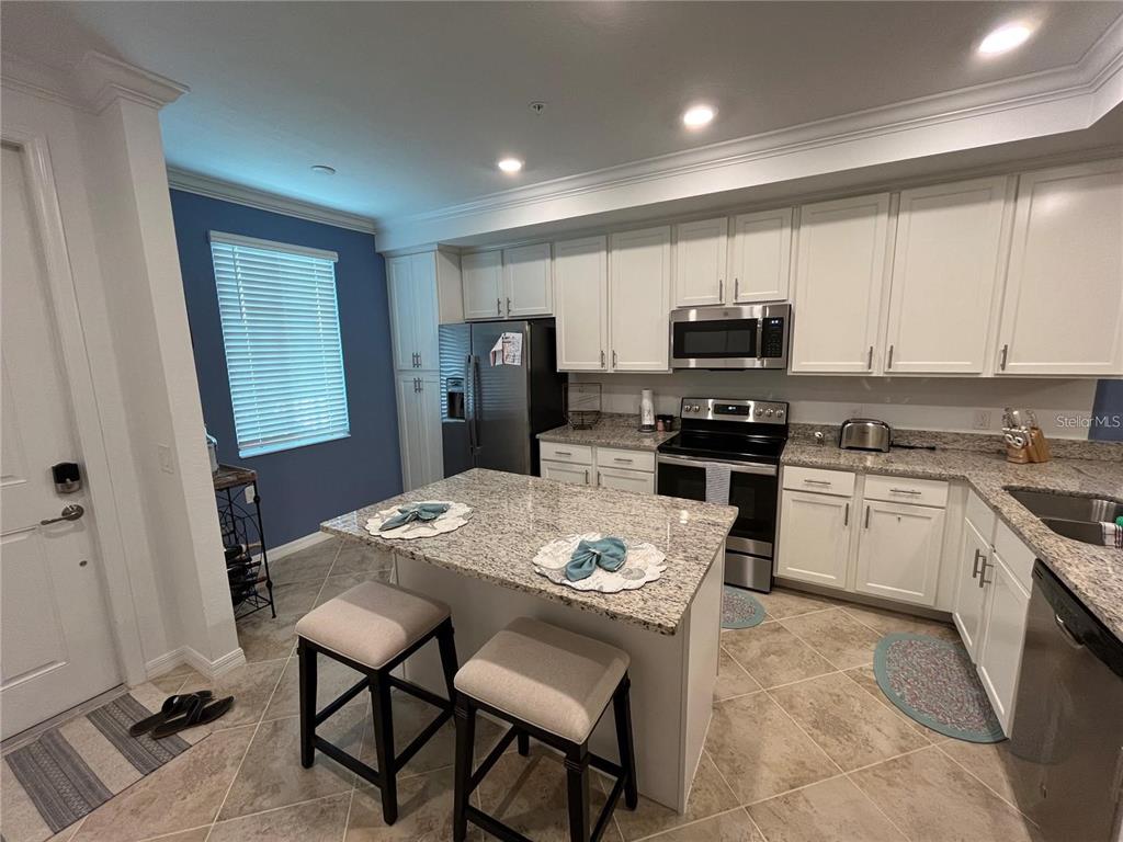 A kitchen features white cabinets, granite countertops, a center island with stools, and tile flooring — 14091 HERITAGE LANDING BOULEVARD UNIT 124, PUNTA GORDA, FL