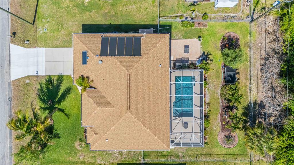 An aerial view shows a house with a shingled roof, solar panels, and a screened pool — 18204 ACKERMAN AVENUE, PORT CHARLOTTE, FL