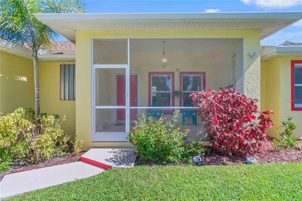 A yellow house features a screened-in front porch with a pink door and landscaping — 18204 ACKERMAN AVENUE, PORT CHARLOTTE, FL