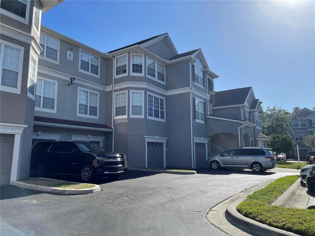 A multi-story gray apartment building with attached garages and parked vehicles in the driveway — 3325 S KIRKMAN ROAD UNIT 420, ORLANDO, FL
