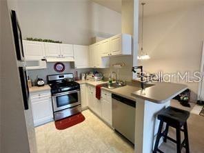 A kitchen features white cabinets, stainless steel appliances, and a breakfast bar with a stool — 3325 S KIRKMAN ROAD UNIT 420, ORLANDO, FL